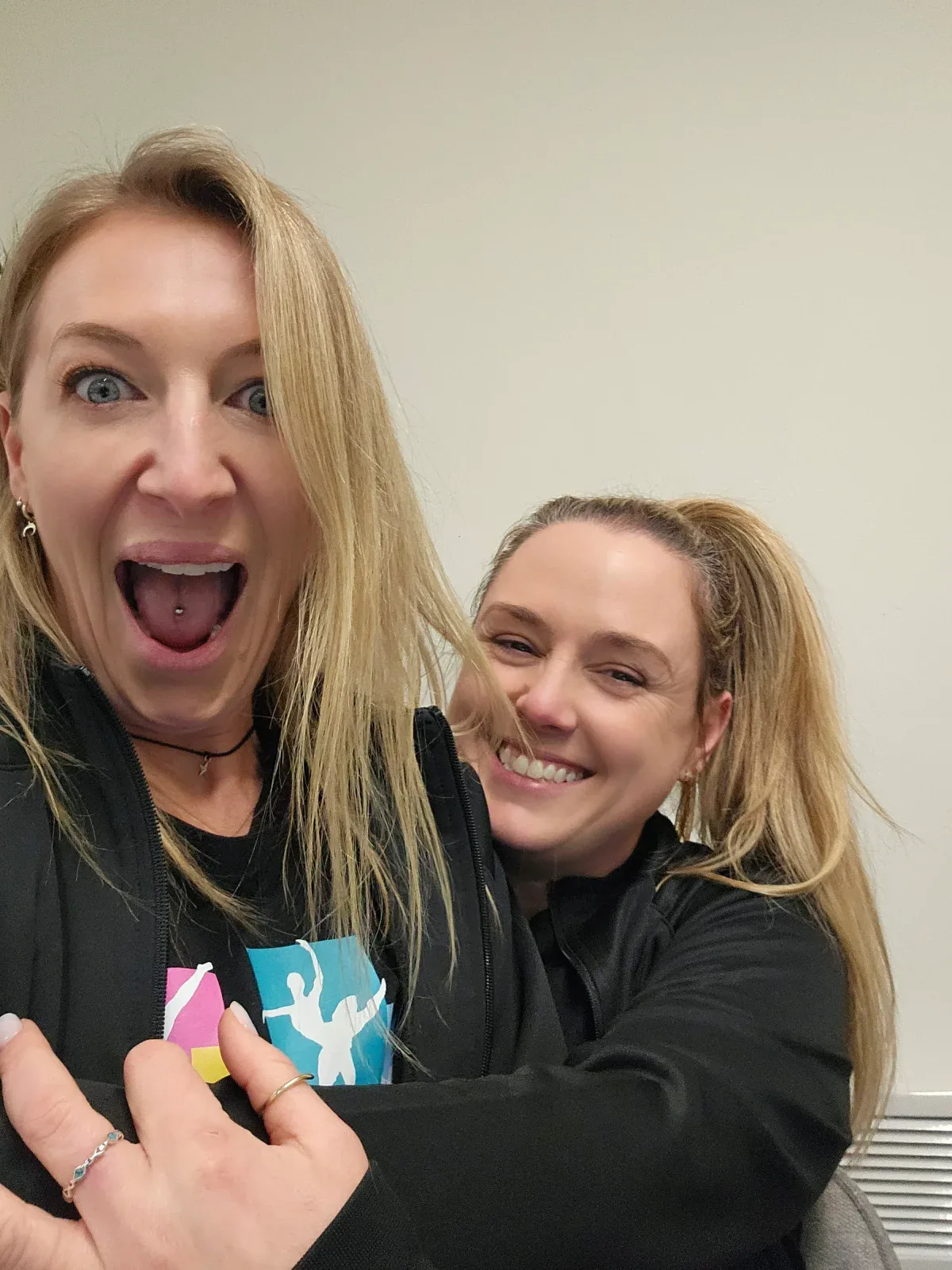 Two women posing together, one holding a school of dance logo